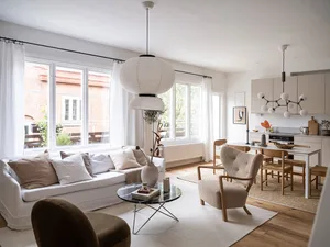 A modern, neutral-toned living room with a comfortable sofa, armchairs, and a dining area in the background.
