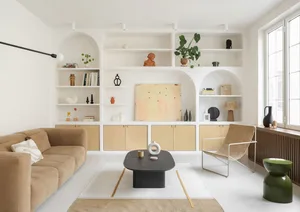 A modern, minimalist living room with beige couches, a black coffee table, and white walls adorned with shelves and plants.