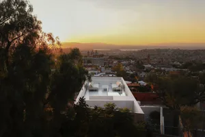 A rooftop with white furniture overlooking a city under a sunset sky.