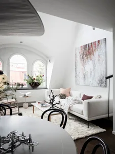 A modern, minimalist living room with a large white sofa, arched windows, and an abstract painting.