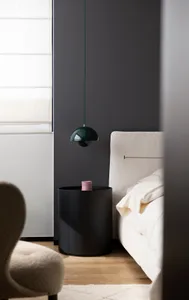 Minimalist bedroom with a white bed and a dark cylindrical bedside table with a pink candle.