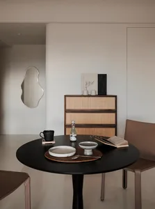 A minimalistic dining room featuring a black dining table with wooden accents and a decorative cabinet in the background.