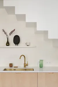 A modern minimalist kitchen features a brass faucet, wood cabinets, and concrete countertops.