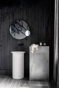 A modern bathroom featuring a minimalist design with concrete walls and a cylindrical pedestal sink.