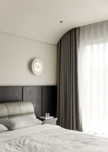 A minimalist bedroom with a gray leather headboard, dark wood-paneled wall, and sheer curtains.