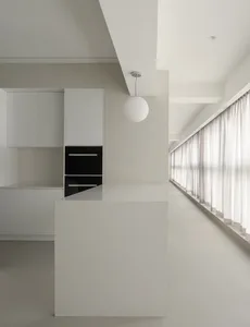 A minimalist residential kitchen with concrete countertops and white cabinets, featuring a cooking area and a long window wit