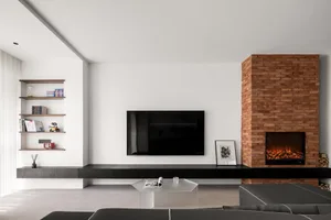 A minimalist living room featuring a flat-screen TV on a floating black shelf, a brick fireplace, and a large sofa.