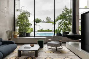 A modern residential living space featuring a pool and greenery through large windows.