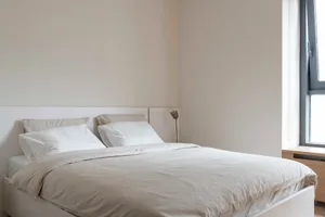 A minimalist bedroom with a bed featuring fabric skips and a neutral color palette.