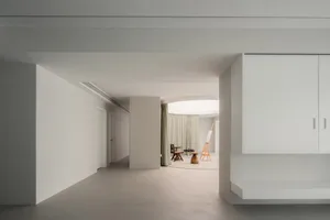 A minimalist living room with a concrete floor, minimalist furniture, and large windows with white curtains.