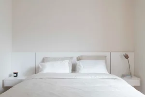 White minimalist bedroom with bed, pillows, and nightstands.