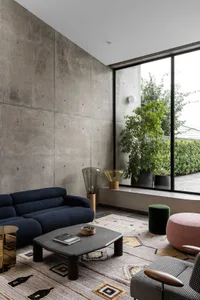 Modern living room with minimalist furniture, concrete walls, and large window.