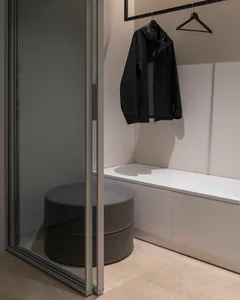 A modern minimalist closet with a glass sliding door, a white counter, and a black jacket hanging on a black hanger.