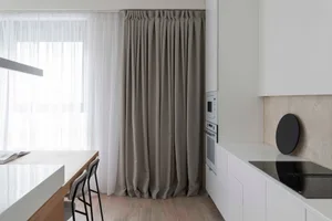 Modern minimalist kitchen featuring white cabinets, beige flooring, and a sleek, minimalist design with a single large window
