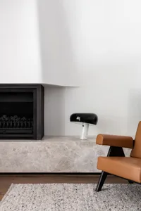 Modern interior design featuring a marble fireplace surround, a black and marble table lamp, and a brown leather armchair wit