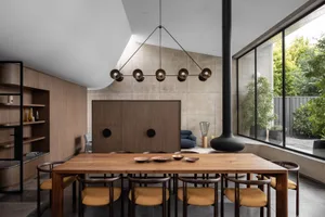 A modern dining room with a wooden dining table and chairs, concrete walls, and a large window.