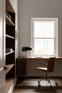 A modern home office with a desk, chair, and lamp next to a bookshelf.