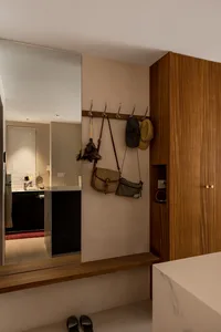 A minimalist entryway featuring a wall-mounted wooden coat rack with bags and hats, a marble bench, and a mirror reflecting a