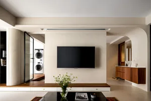 A modern minimalist living room featuring concrete walls, a black flat-screen TV, and a small glass vase with white flowers.