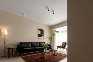Modern minimalist living room with black leather sofa, glass coffee table, and abstract artwork.