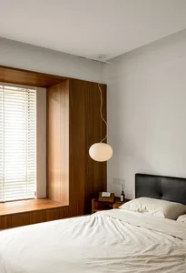 A minimalist bedroom with wooden walls, a bed, and a spherical hanging light fixture.