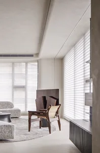 A minimalist living room with neutral-toned furniture, a rug, and large windows with blinds.