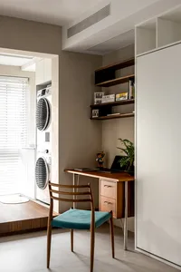 A minimalist home office setup with a wooden desk and chair, featuring a small shelf with books and plants, a clothes wardrob