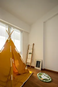 A yellow children's play tent set up indoors with a ladder, rug, and window with blinds.