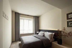 A minimalist bedroom with neutral-colored walls, curtains, and bedding, featuring a large window and a cozy bed setting.