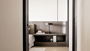A minimalist bedroom featuring a wooden bed frame, books, and a small table lamp on a wooden shelf.
