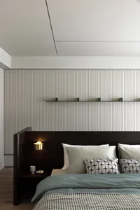 A modern minimalist bedroom with a wooden headboard, fabric bedding, and metallic accents on the nightstand and shelves.