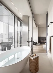 Modern minimalist bathroom with glass and porcelain materials, featuring a freestanding bathtub and a view of the cityscape t