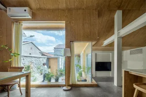 A minimalist living room with wooden walls and floors, featuring a floor lamp, a dining table, and window with a view of gree