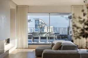 Modern living room with gray fabric seating, large windows, and cityscape view.