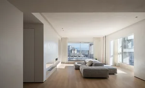 A minimalist living room with modern furniture and white walls, featuring a large window with a view of the city.