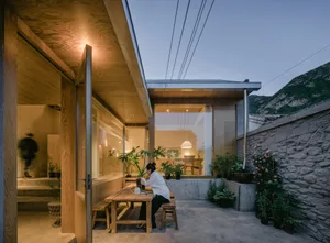A modern residential exterior featuring wooden structures, glass windows, and concrete elements.