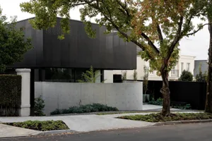 Modern black concrete residential exterior with glass windows and a concrete driveway.