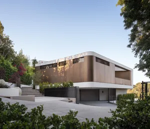 Modern residential exterior with wooden panels, glass windows, and concrete driveway.