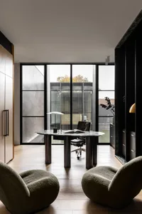 Modern home office featuring a marble desk and black chairs with a floor-to-ceiling window overlooking a garden.