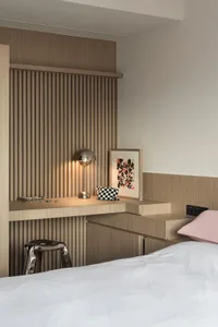 A modern minimalist bedroom with wooden walls and a white bedspread, featuring a built-in desk and artwork.