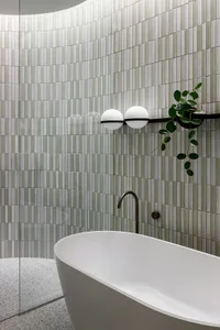 A modern bathroom featuring green ceramic tiles and a freestanding bathtub, with minimalistic lighting and plant decor.