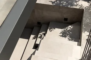 A minimalist concrete space featuring a set of stairs with shadows of trees.