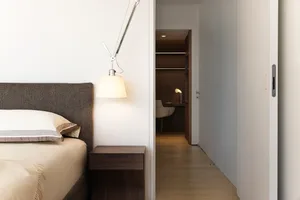 A modern minimalist bedroom with a wooden floor and a bed covered in fabric.