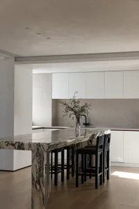 Modern minimalist kitchen with marble countertops and black stools.