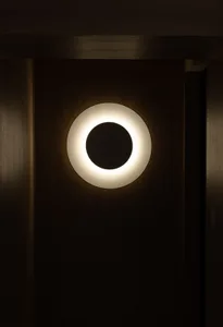 A minimalist wall light fixture with a white circular design and a metal finish.