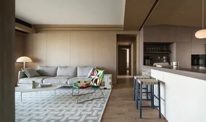 Modern living room with wooden walls and a comfortable seating area, featuring a patterned rug and colorful chairs.
