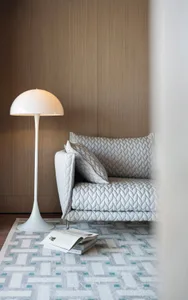 A cozy living room with a light gray sofa, a white floor lamp, and an open book on a patterned rug.