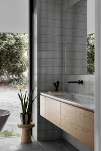 Modern bathroom with a geometric tiled wall, marble sink counter, and wooden cabinet.