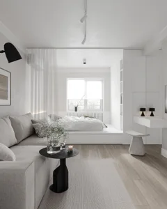 Modern minimalist bedroom with white furniture, wood flooring, and a window with sheer curtains.
