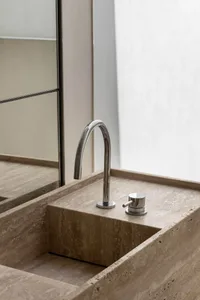 A minimalist, marble bathroom sink with a sleek, curved faucet and two-handle controls.